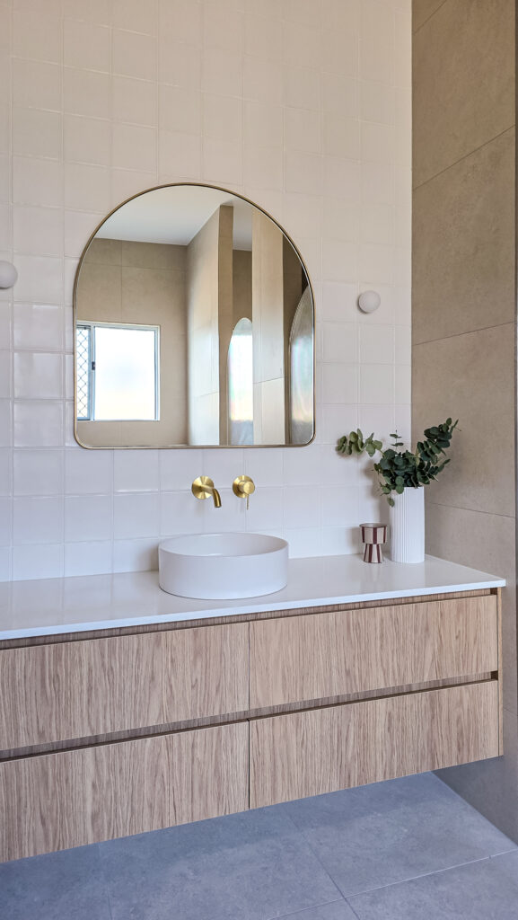 Bathroom with an arched mirror, white vessel basin and timber vanity