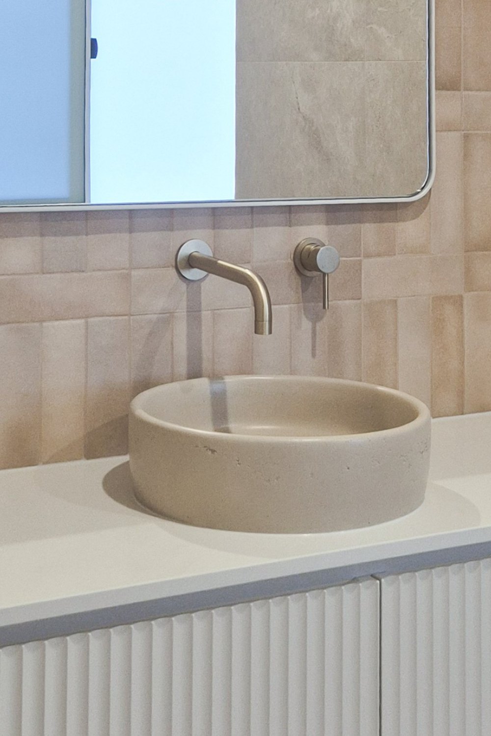 Stone-look round basin on a white vanity with brushed tapware