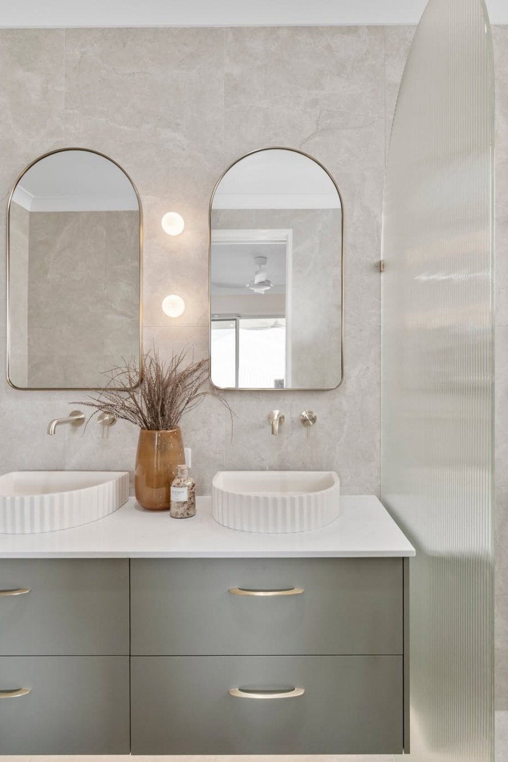Bathroom with large format wall tiles, arched mirrors and a sage vanity